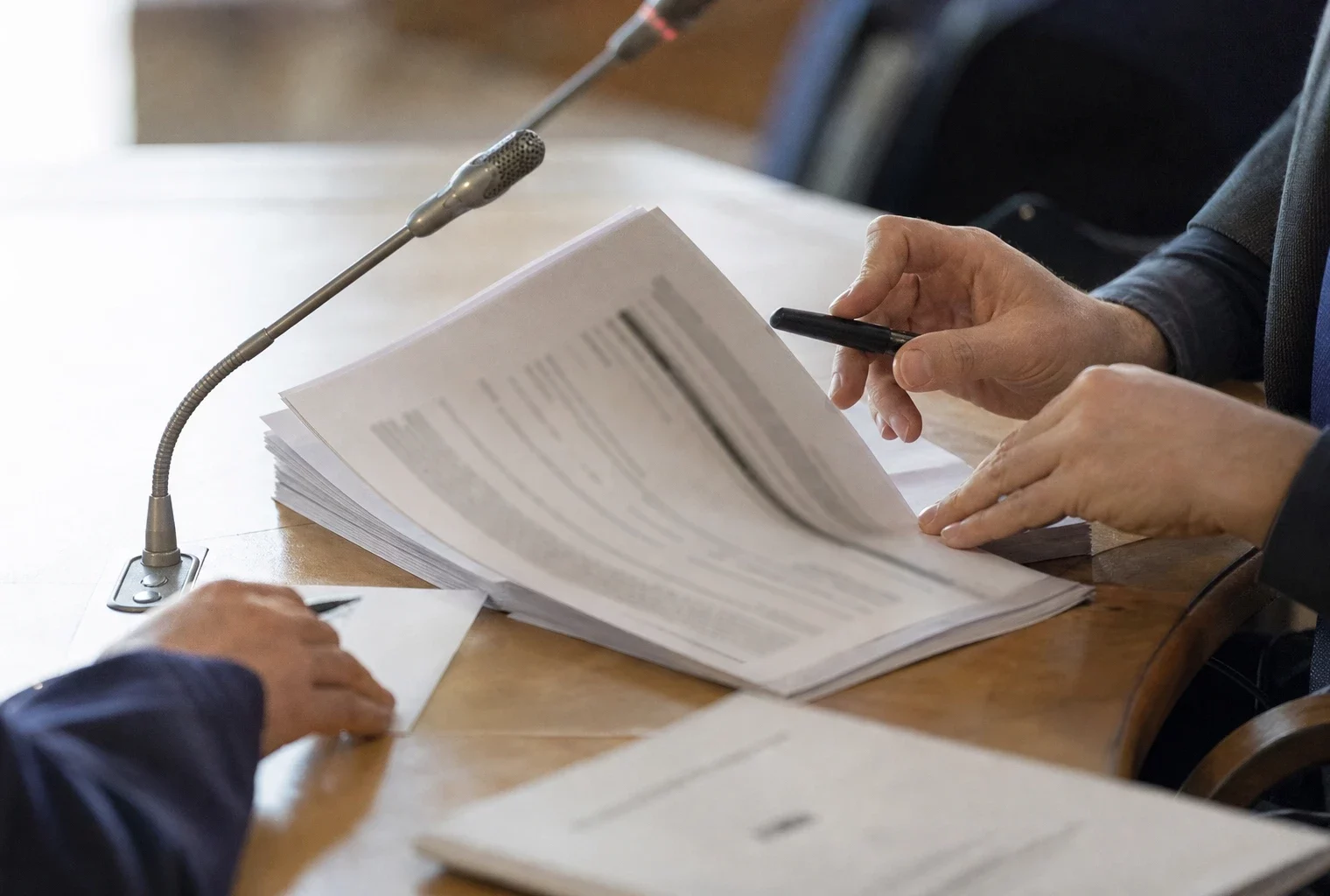 Mains anonymes examinant un dossier d’audition près d’un micro de commission parlementaire en France