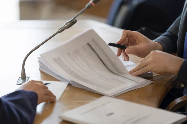 Mains anonymes examinant un dossier d’audition près d’un micro de commission parlementaire en France