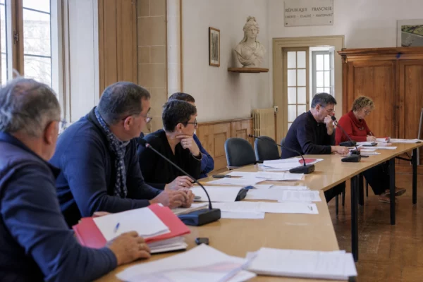 Salle municipale française avec une chaise vide, des micros et des dossiers lors d’un conseil local