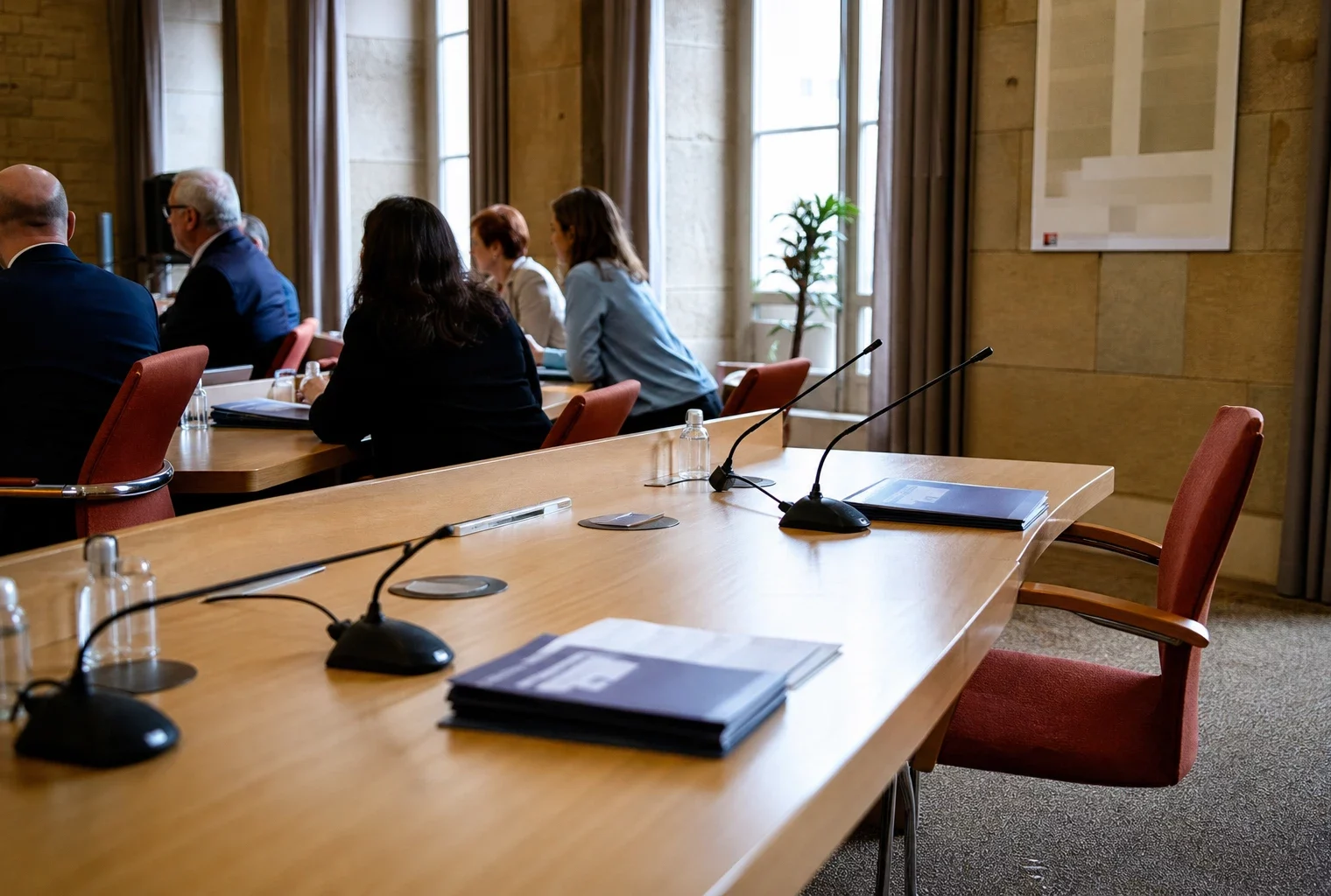 Salle de conseil municipal française avec une chaise vide, des micros et des dossiers flous autour d’une table