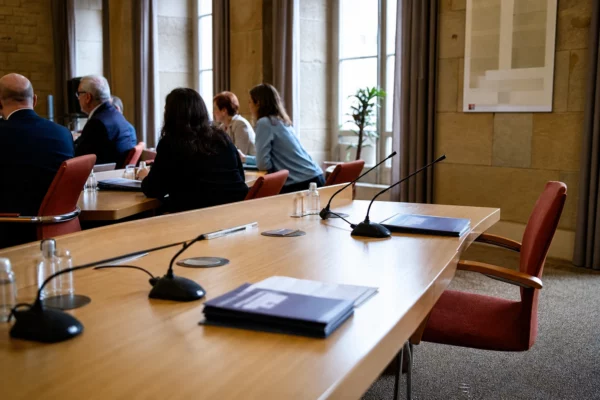 Salle de conseil municipal française avec une chaise vide, des micros et des dossiers flous autour d’une table