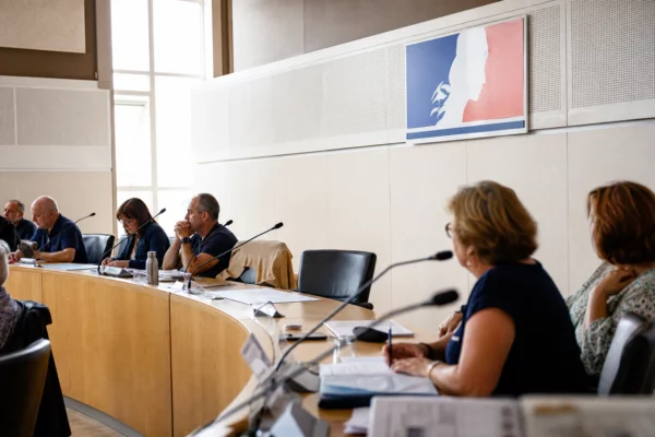 Salle de conseil municipal française avec une chaise vide, des micros et des dossiers lors d’une réunion locale