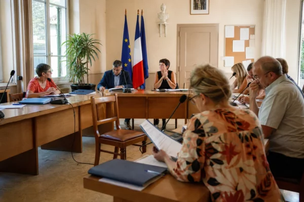 Salle municipale française réunie autour de l’adaptation climatique, avec micros, dossiers et une chaise vide