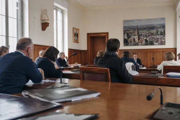 Salle de conseil municipal française avec chaise vide, micros et dossiers lors d’un débat politique international