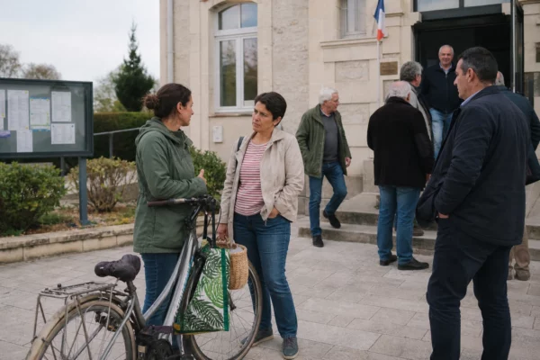 Citoyens anonymes devant une mairie française, échangeant sur les effets économiques de la crise d’Ormuz