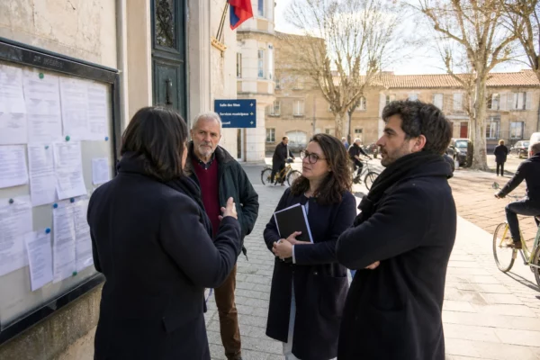 Habitants anonymes échangeant sur une place de ville française près d’un bâtiment municipal, en lumière naturelle