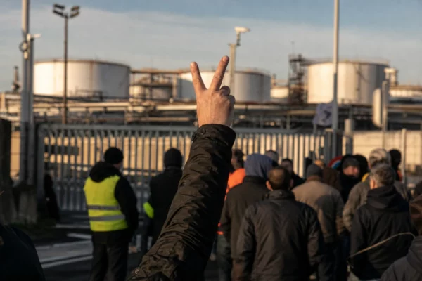 Des manifestants bloquent l’entrée d’un dépôt pétrolier, avec les cuves et tuyauteries visibles derrière.