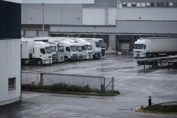 Dans un dépôt de transport routier, plusieurs camions stationnés devant un hangar logistique et des quais de chargement.