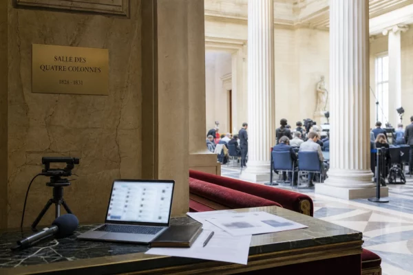 Salle parlementaire française avec caméra de presse et écran flou évoquant la surveillance de la désinformation numérique