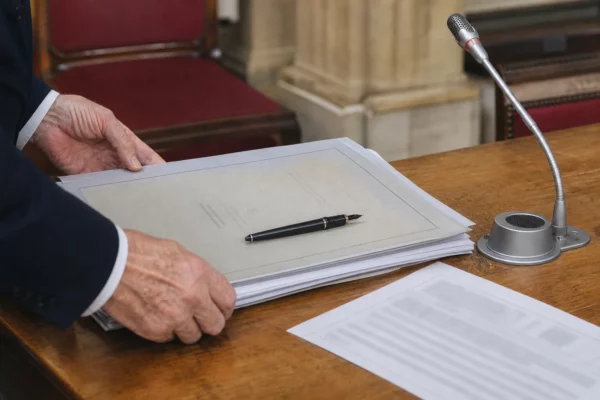 Mains anonymes examinant un dossier de nomination près d’un micro dans une salle de commission française
