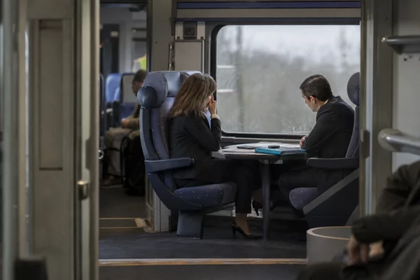 Dans un train, deux personnes échangent autour de documents posés sur une tablette.
