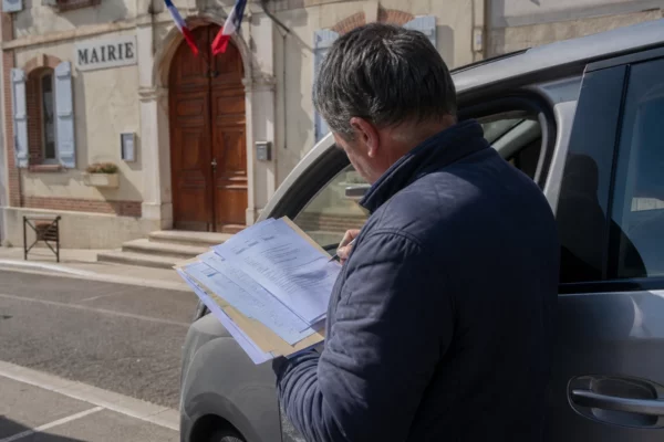 Élu local anonyme consultant un dossier sur les prix du carburant devant une mairie française