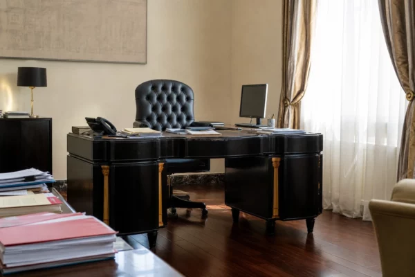 Bureau sobre de l’Élysée avec fauteuil noir, dossiers et téléphone, baigné par une lumière douce de fenêtre.