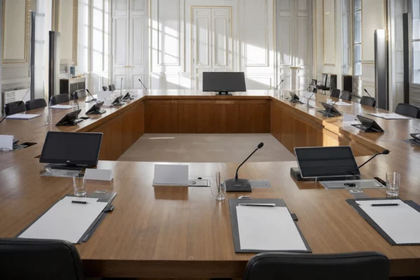 Salle de conférence de l’Élysée vide, table en U, micros et dossiers vierges sous une lumière matinale claire.