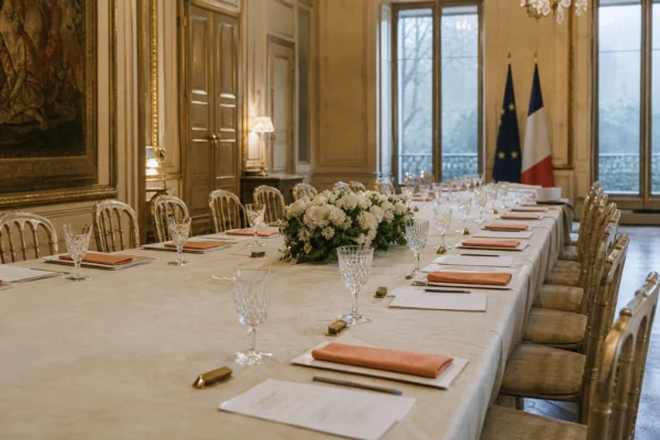 Salon de réception de l’Élysée avec grande table dressée, fauteuils alignés et boiseries sobriaux sous une lumière grise.