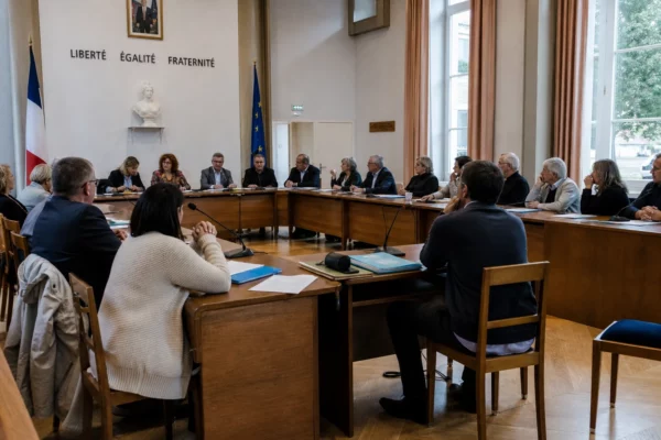 Conseil municipal français sur l’encadrement des loyers, avec micros, dossiers flous et une chaise vide