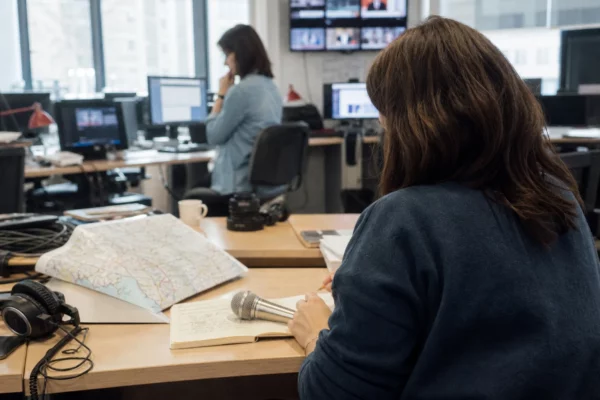 Journaliste préparant un sujet politique territorial dans une rédaction locale, avec carnet, carte papier et micro sans logo