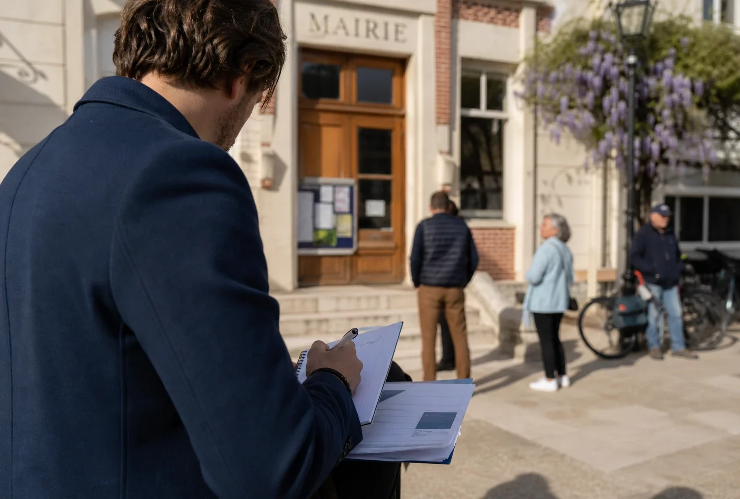 Collaborateur politique anonyme prenant des notes devant une mairie française, dans une scène de campagne locale