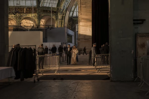 Entrée nocturne du Grand Palais, couple élégant au centre, barrières et hall d’événement sous la verrière