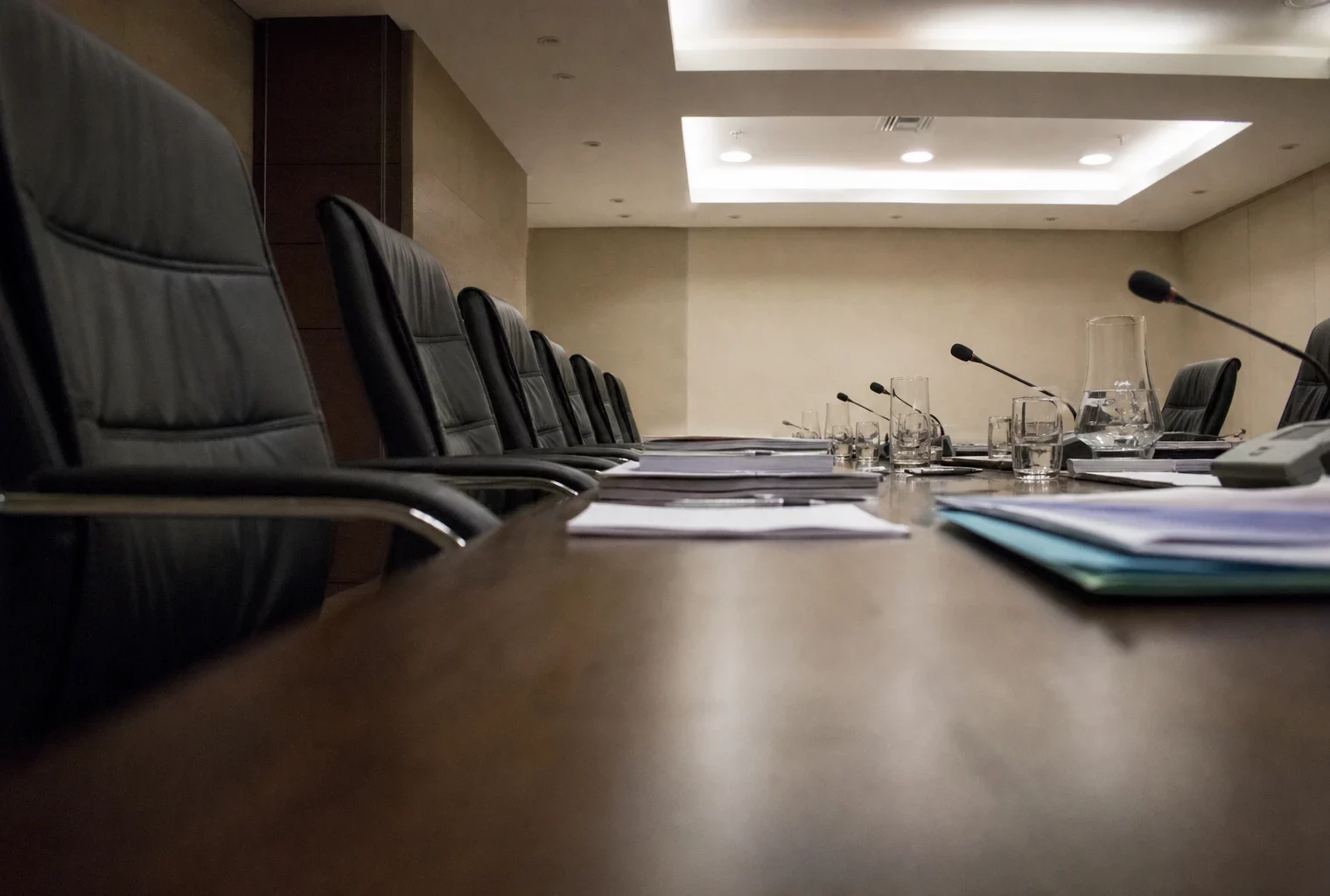 Salle de réunion parlementaire sobre au Sénat, tables alignées, micros, dossiers et sièges vides sous une lumière diffuse.