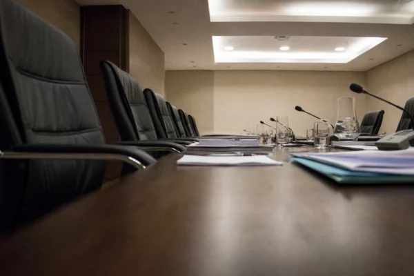 Salle de réunion parlementaire sobre au Sénat, tables alignées, micros, dossiers et sièges vides sous une lumière diffuse.