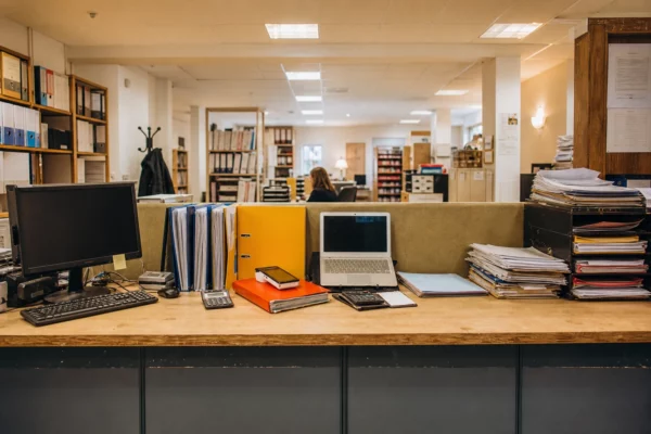 Guichet administratif français vu en largeur, comptoir de service, dossiers, ordinateur et classeurs sous lumière chaude.