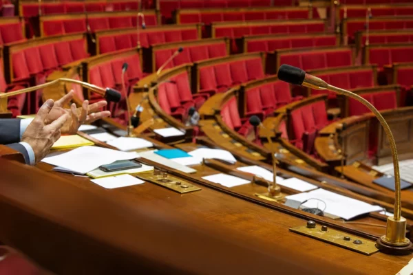 Hémicycle de l’Assemblée nationale avec ses pupitres et sièges, vu vide dans un décor parlementaire ordinaire.