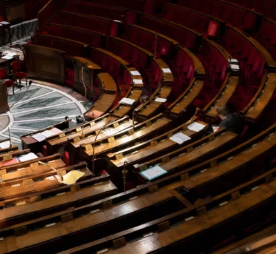 L’hémicycle de l’Assemblée nationale avec ses pupitres et ses micros, dans un cadre institutionnel sobre.
