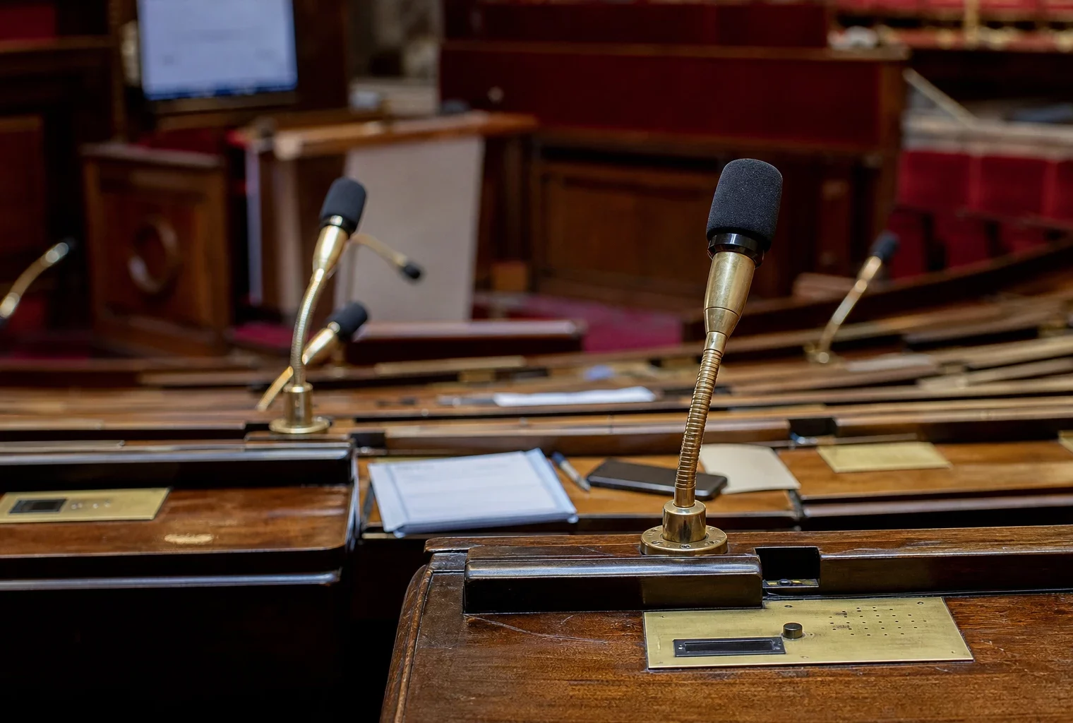 Hémicycle de l’Assemblée nationale vide avec rangées de pupitres et micros de vote.