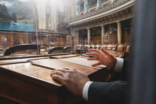 Main dans l’hémicycle d’un conseil régional, sur fond de pupitres, micros et gradins de l’assemblée.
