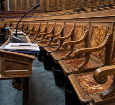 Hémicycle du Sénat vide, avec bancs de bois sculpté, pupitres et micros, sous une lumière naturelle douce.