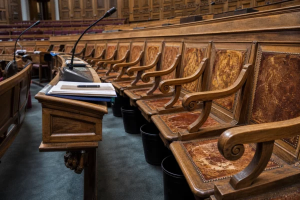 Hémicycle du Sénat vide, avec bancs de bois sculpté, pupitres et micros, sous une lumière naturelle douce.