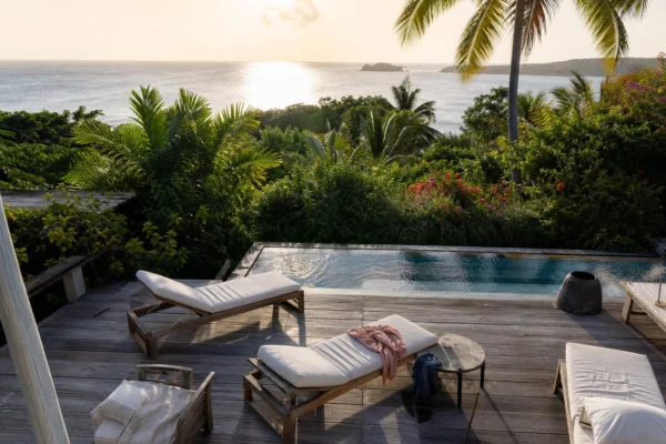 Villa de vacances isolée sur une île tropicale, avec terrasse en bois, transats et végétation dense.