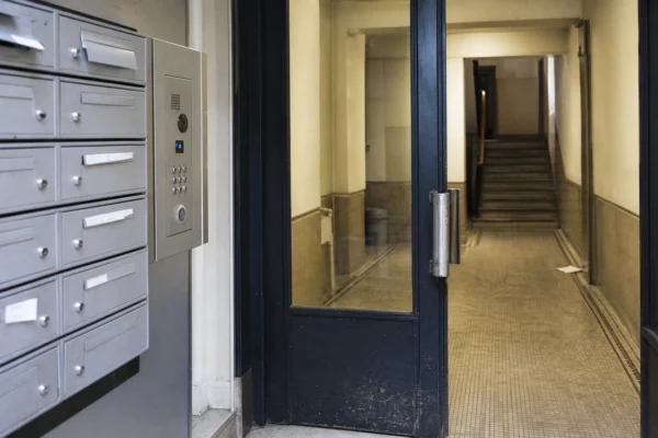 Entrée d’immeuble résidentiel avec boîtes aux lettres et interphone, pour illustrer le poids du loyer sur le budget des retraités.