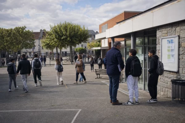 Scène de cour d’école française avec un enseignant échangeant avec des élèves dans un cadre quotidien et apaisé