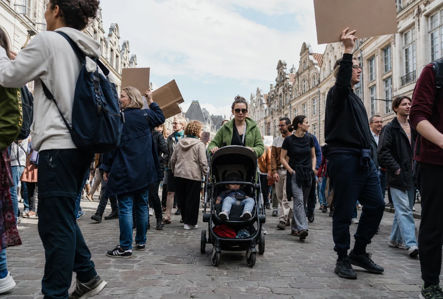 Landau au centre d’une marche pour le climat à Arras, poussé parmi des manifestants et des pancartes, façades de rue en fond.