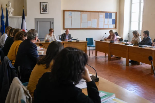 Salle municipale française avec chaise vide, micros et dossiers lors d’un débat sur la protection des enfants
