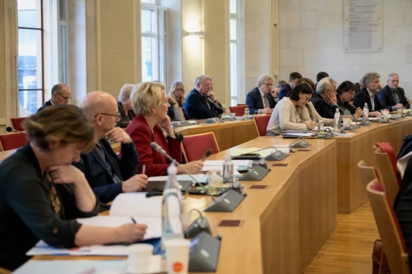 Salle municipale française avec micros, dossiers flous et chaise vide lors d’un débat institutionnel sur les violences