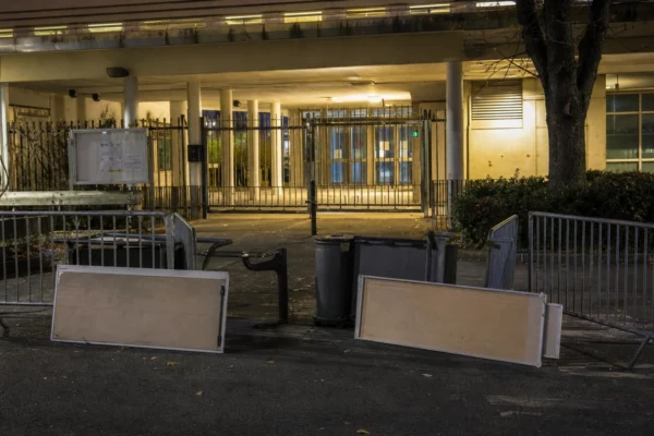 Entrée d’un lycée public bloquée par des barrières, avec le portail fermé et du mobilier déplacé.