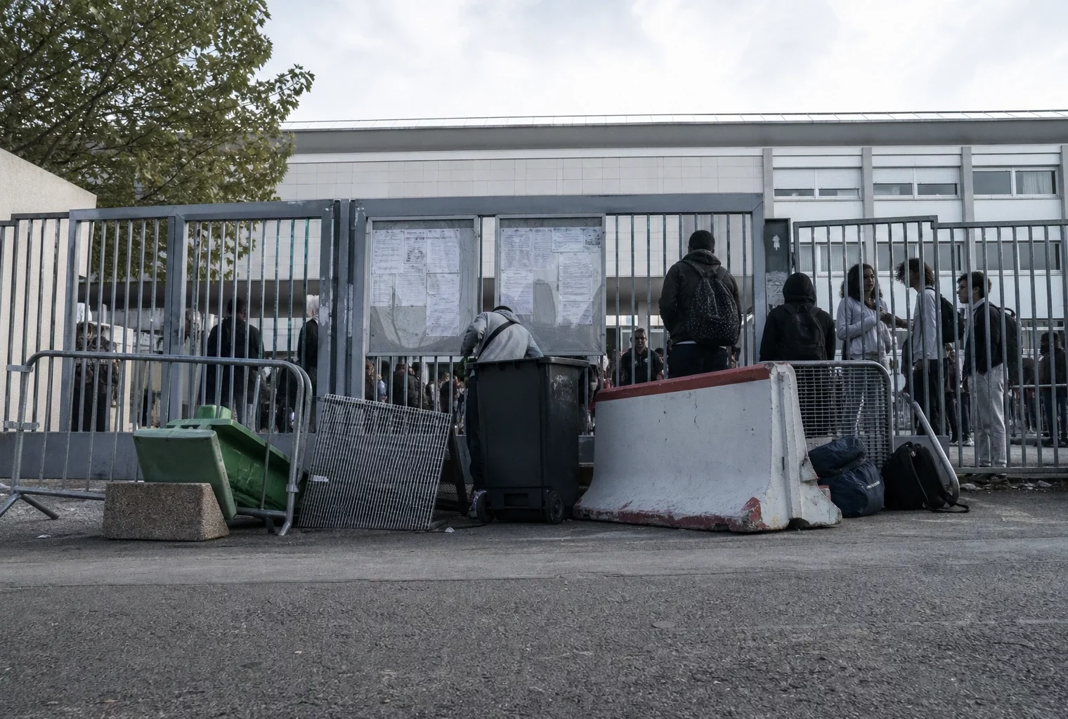 Entrée d’un lycée bloquée par des élèves mobilisés, avec barrières et groupes d’étudiants devant le portail.