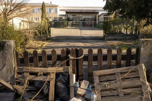 Portail de lycée fermé par un barrage improvisé, avec grilles verrouillées, palettes et sacs devant l’entrée en hiver.