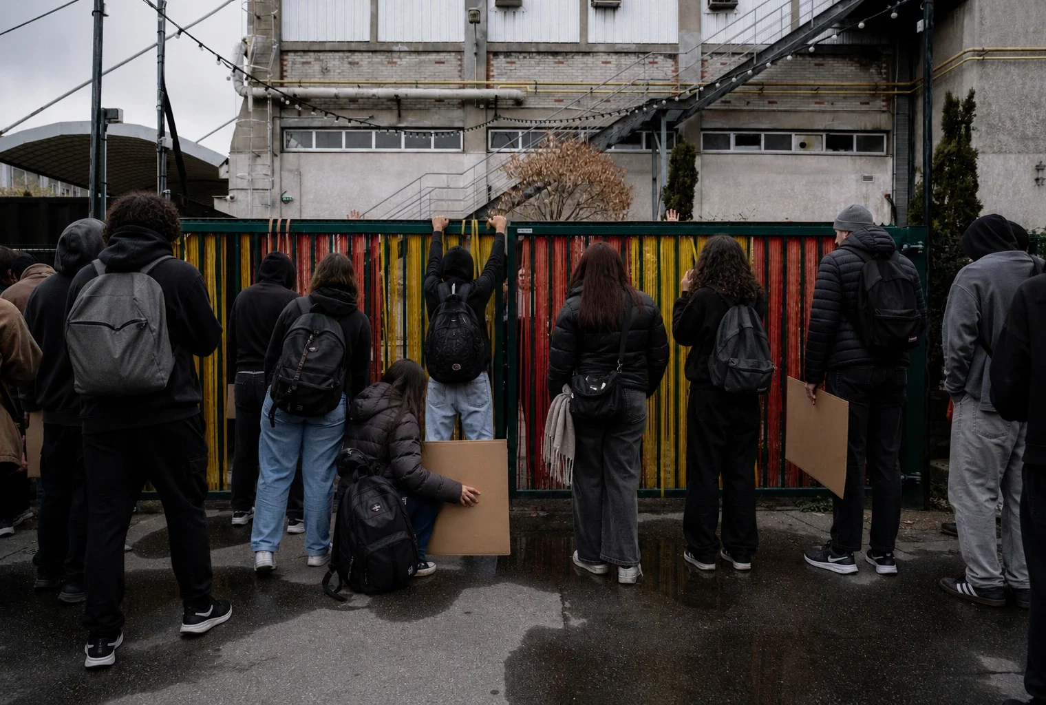 Des élèves bloquent la grille d’un lycée à Saint-Denis, sacs et pancartes, devant la façade et le trottoir humide.