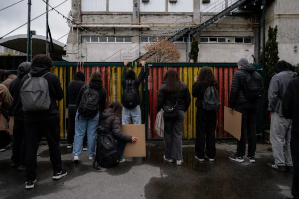Des élèves bloquent la grille d’un lycée à Saint-Denis, sacs et pancartes, devant la façade et le trottoir humide.