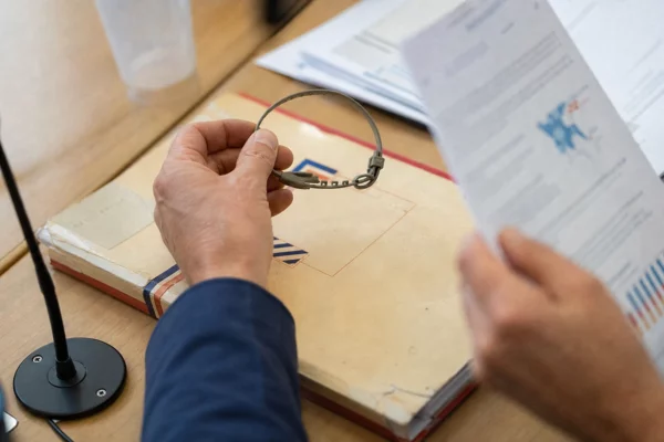 Main tenant un collier antiparasitaire au-dessus d’un dossier politique flou, dans une scène éditoriale française lumineuse