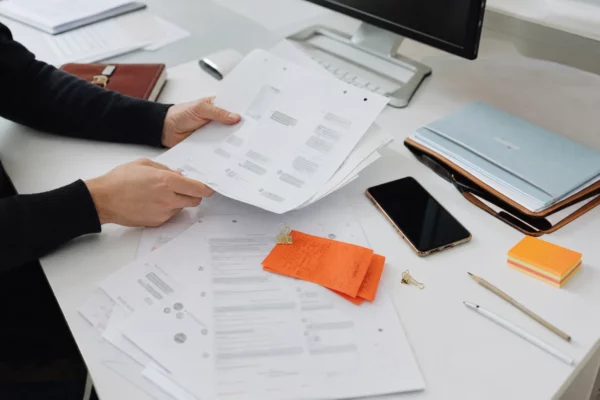 Vue en plongée d’un bureau d’avocat avec feuilles imprimées, téléphone et mains consultant d’anciens échanges.