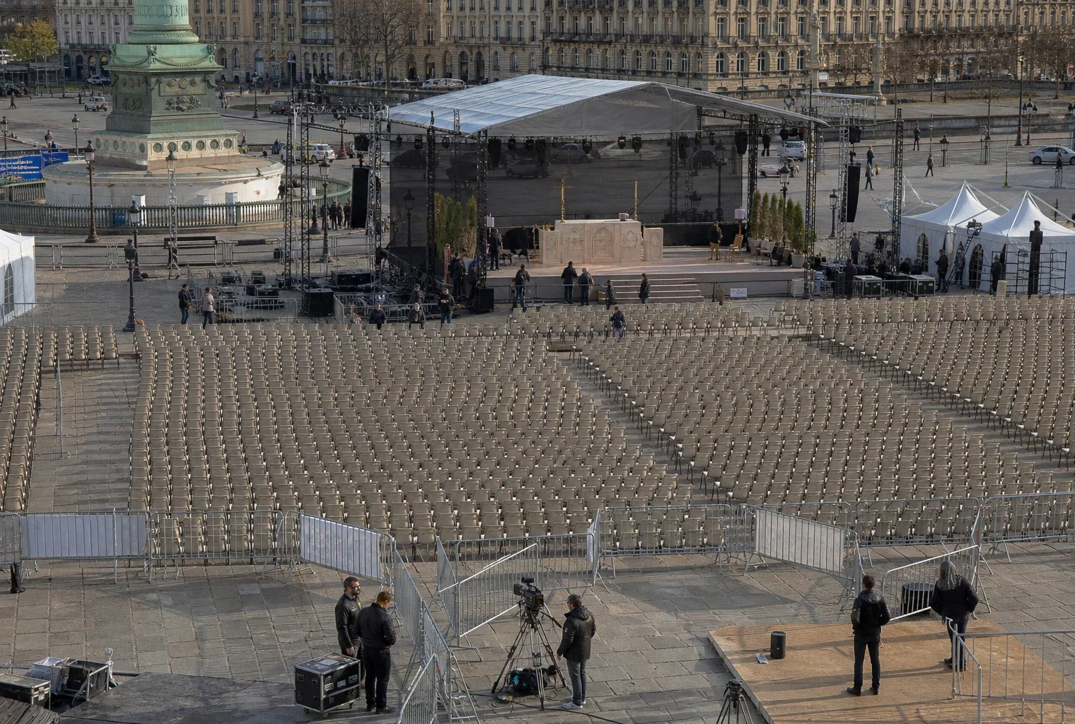 Vue en plongée de rangées de chaises devant une estrade provisoire sur la place de la Concorde, avec façades parisiennes au loin.