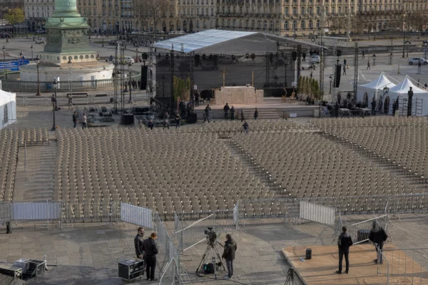 Vue en plongée de rangées de chaises devant une estrade provisoire sur la place de la Concorde, avec façades parisiennes au loin.
