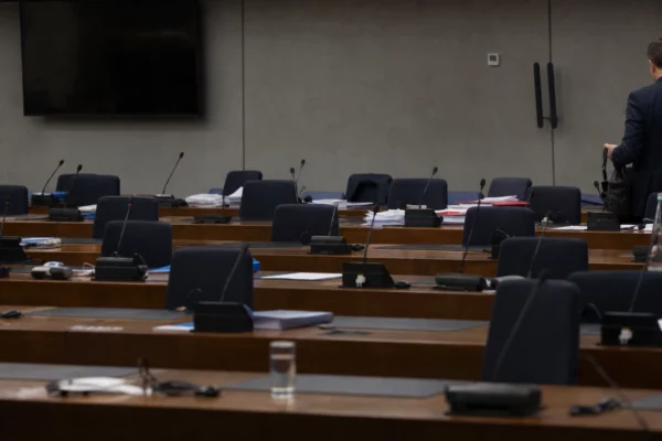Salle de négociation européenne avec pupitres, micros et dossiers, en attente d’une réunion budgétaire.