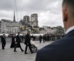 Notre-Dame vue depuis le parvis, avec barrières de sécurité au premier plan et façade de la cathédrale en arrière-plan sous ciel gris.