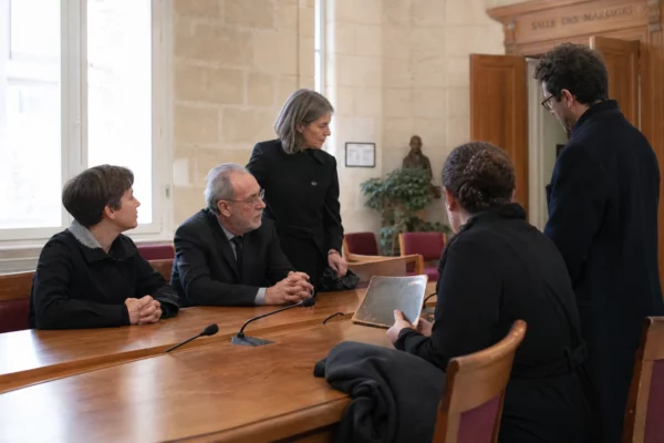 Réunion sobre dans une salle civique française après des obsèques privées, avec proches anonymisés et microphones de presse